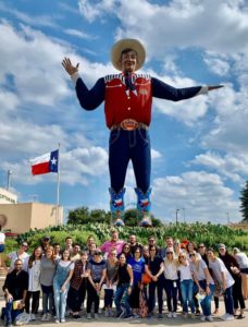 Group of FleishmanHillard Dallas employees at state fair in front of giant cowboy statue and Texas flag