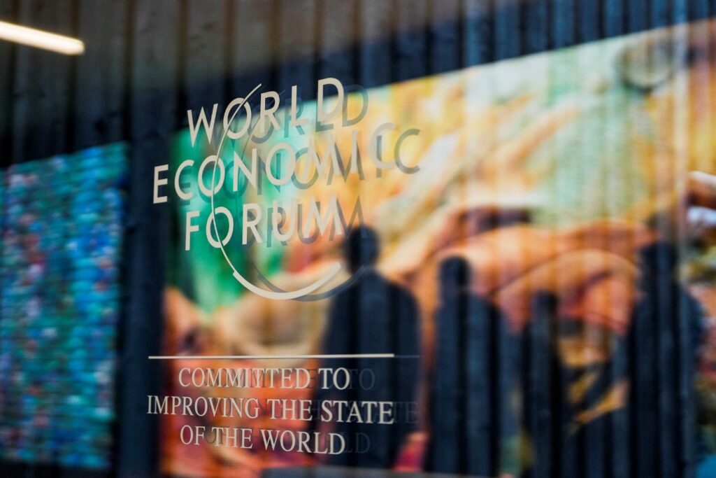 World Economic Forum on a glass wall with the reflection of people walking by